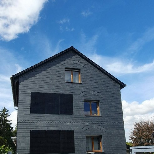Giebelseite mit grauer Fassadenbekleidung und dekorativen Mustern.