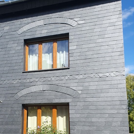 Graue Fassadenbekleidung mit ornamentalen Linien an den Fenstern.